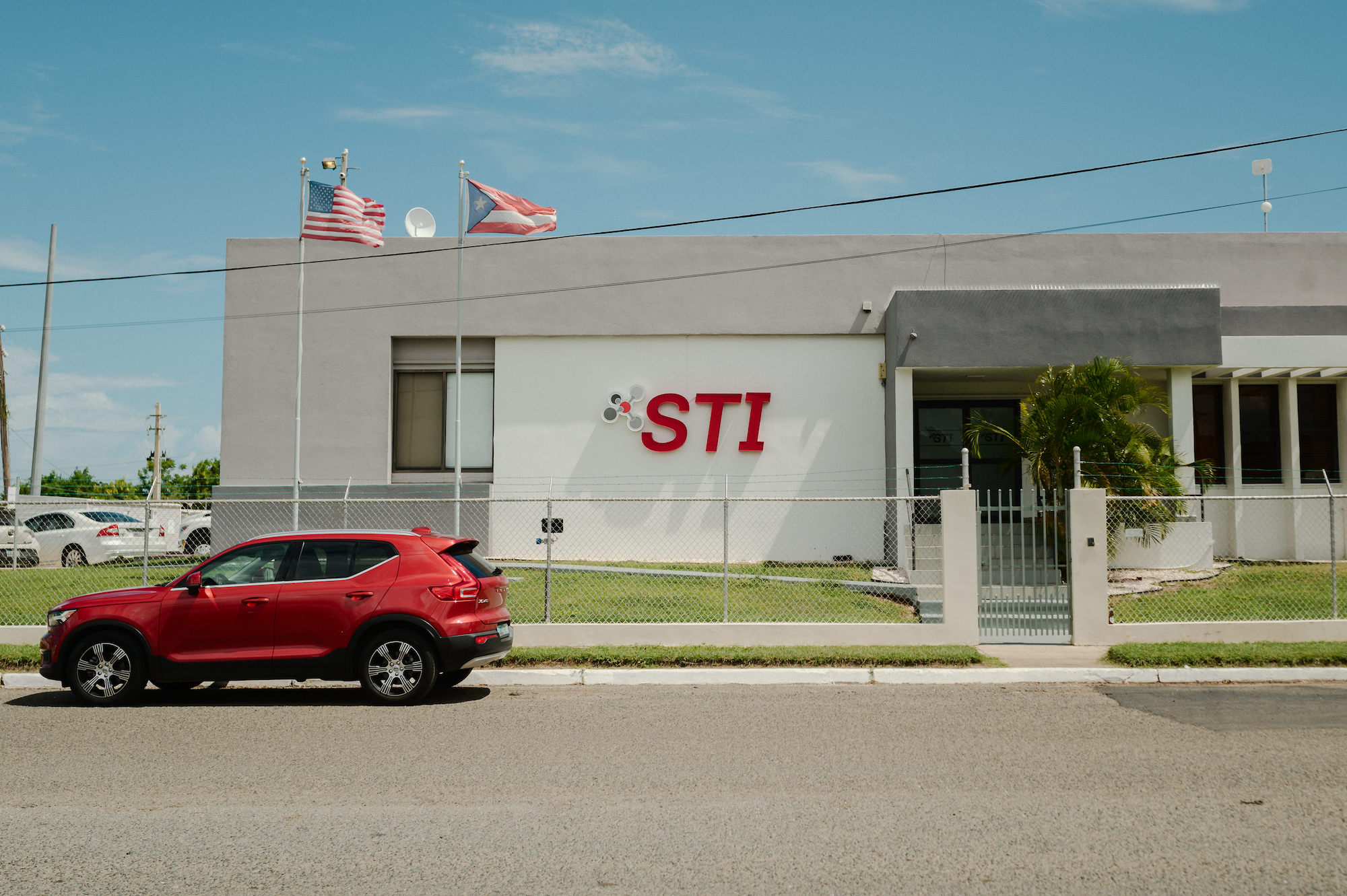 A red car drives past a building that says 'STI' on it in large red letters