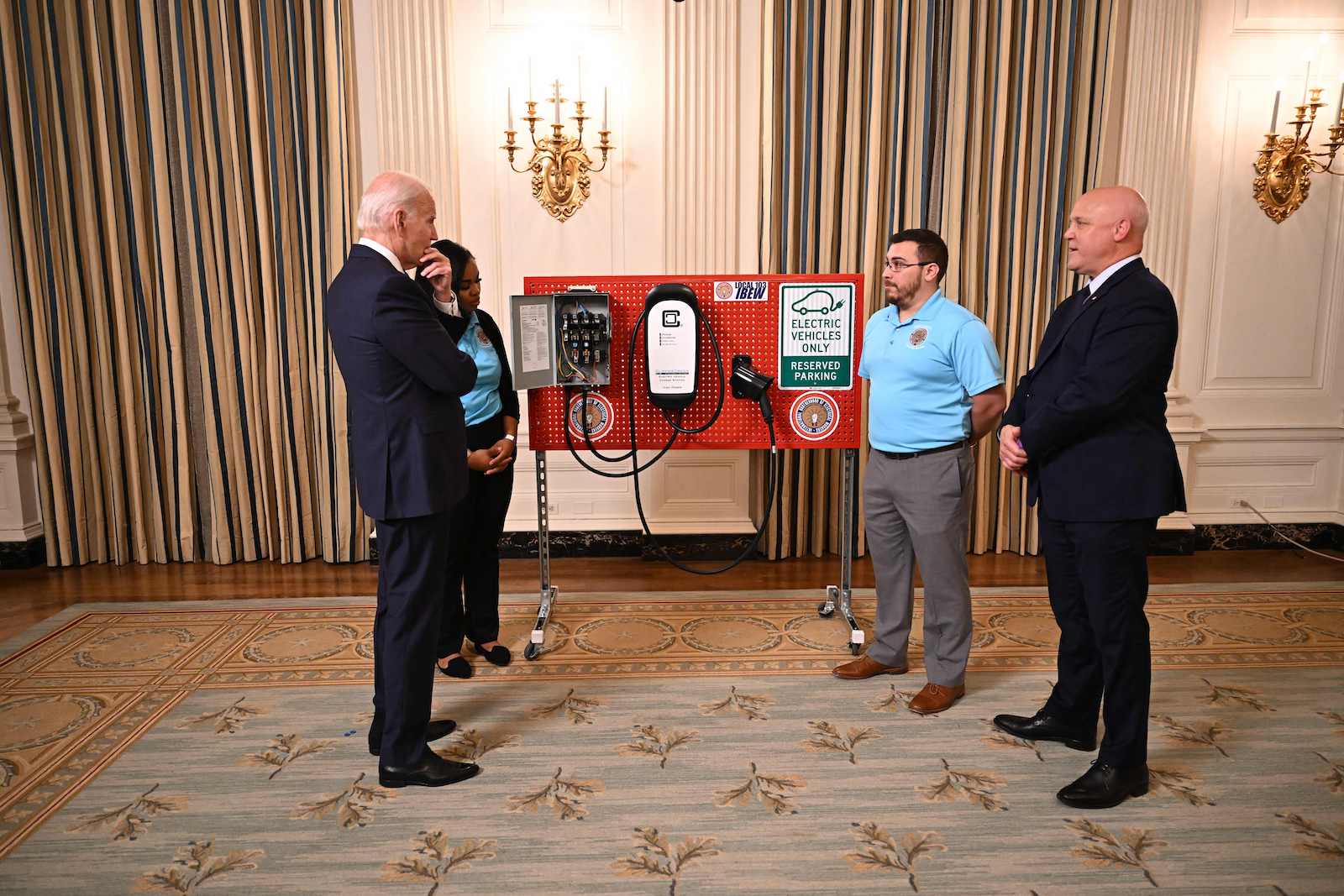 men in suits stand in front of a red display with electric vehicle sign and chargers