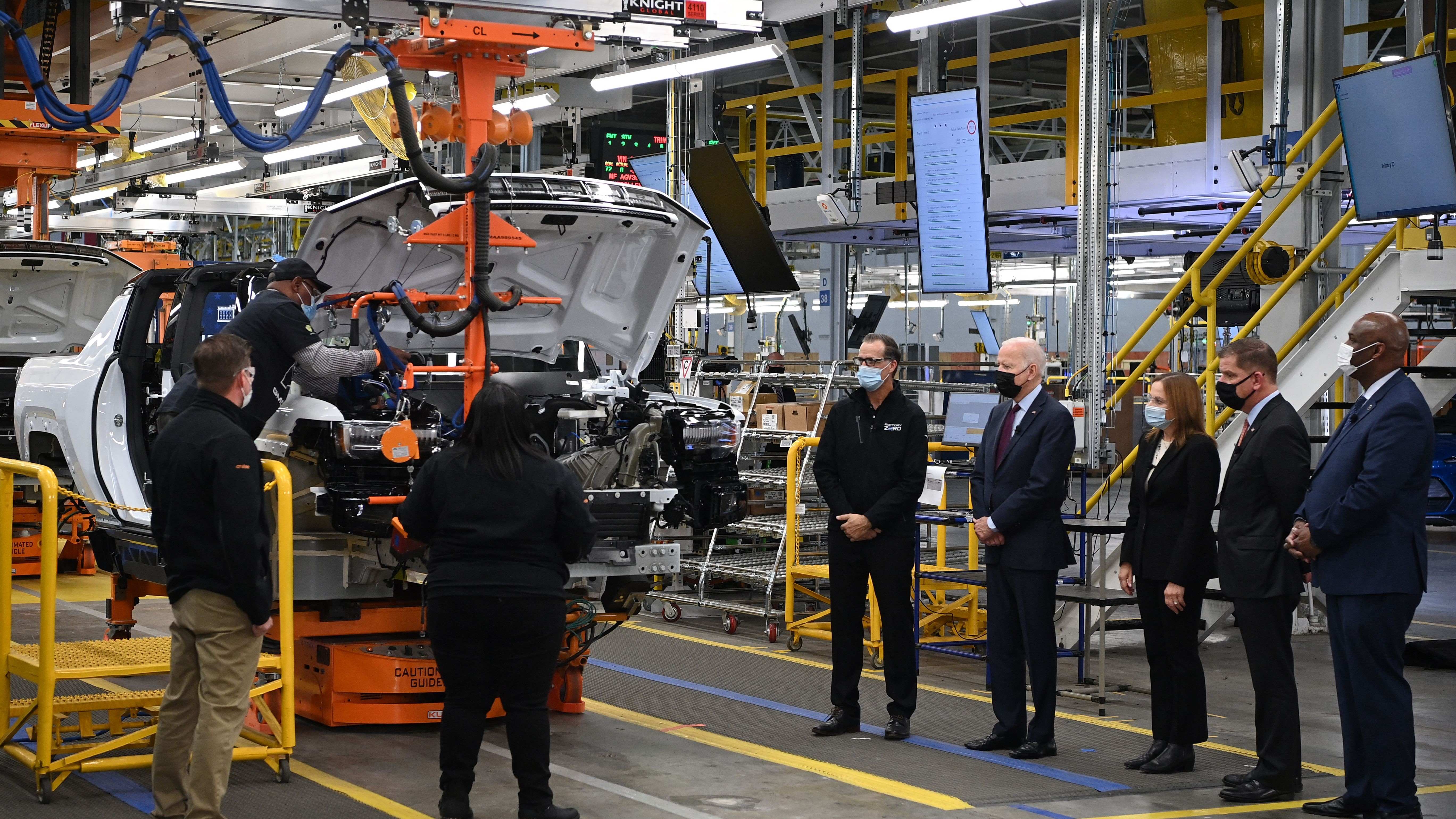 President Joe Biden and others stand on the floor of an EV assembly plant