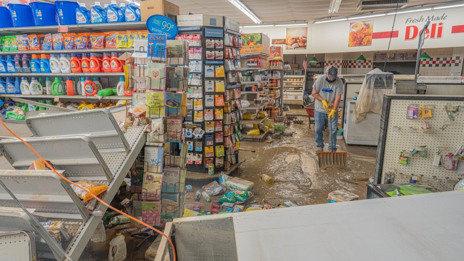 A man with a shovel tries to clean up water that has flooded a grocery store.