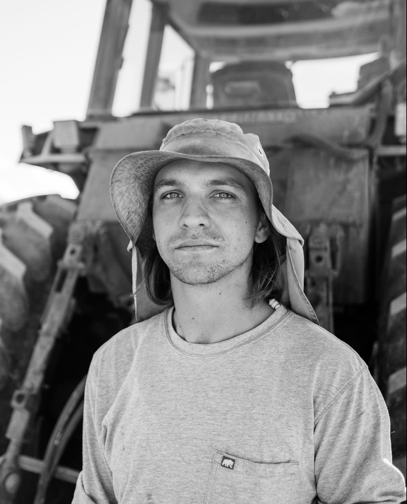 a man in a bucket hat stands in front of a piece of construction equipment