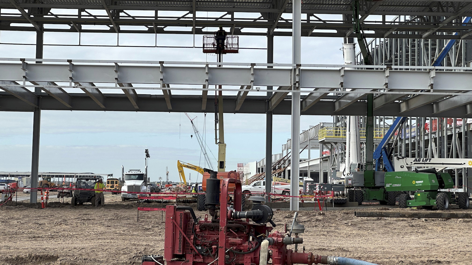 A worker stands on a mechanical lift amid construction on a large building