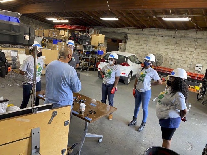 people in gray t-shirts and hard hats stand in a warehouse