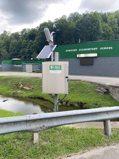 A machine with a small solar panel stands above a stream.